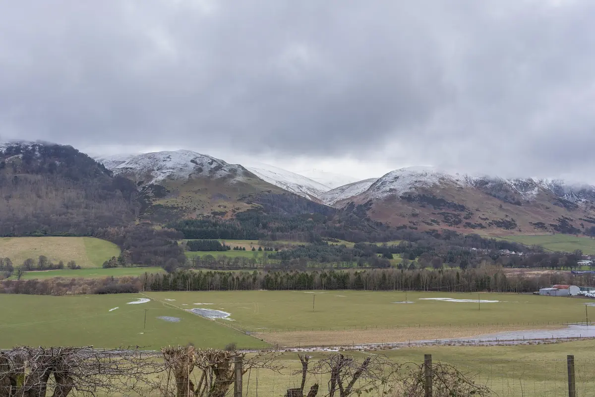 Snow-dusted Ochil Hills beneath heavy grey cloud over the carse fields