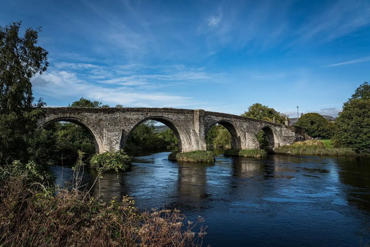 Stone arches of Stirling Old Bridge reflected in the dark River Forth