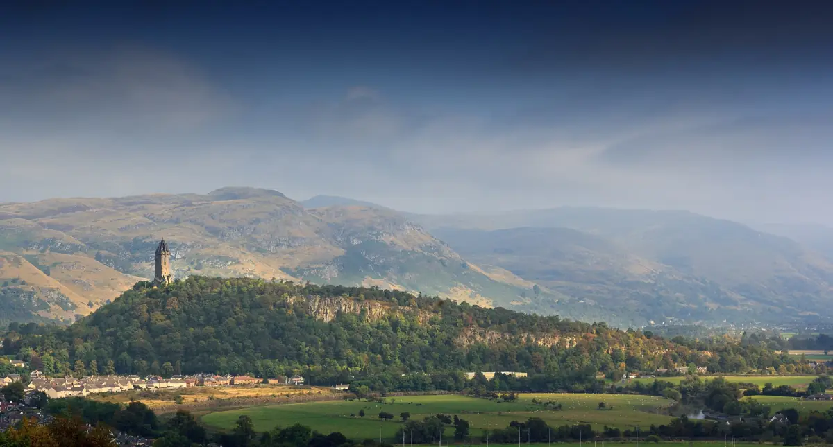 Wallace Monument on its wooded hill with the Ochils in warm evening light